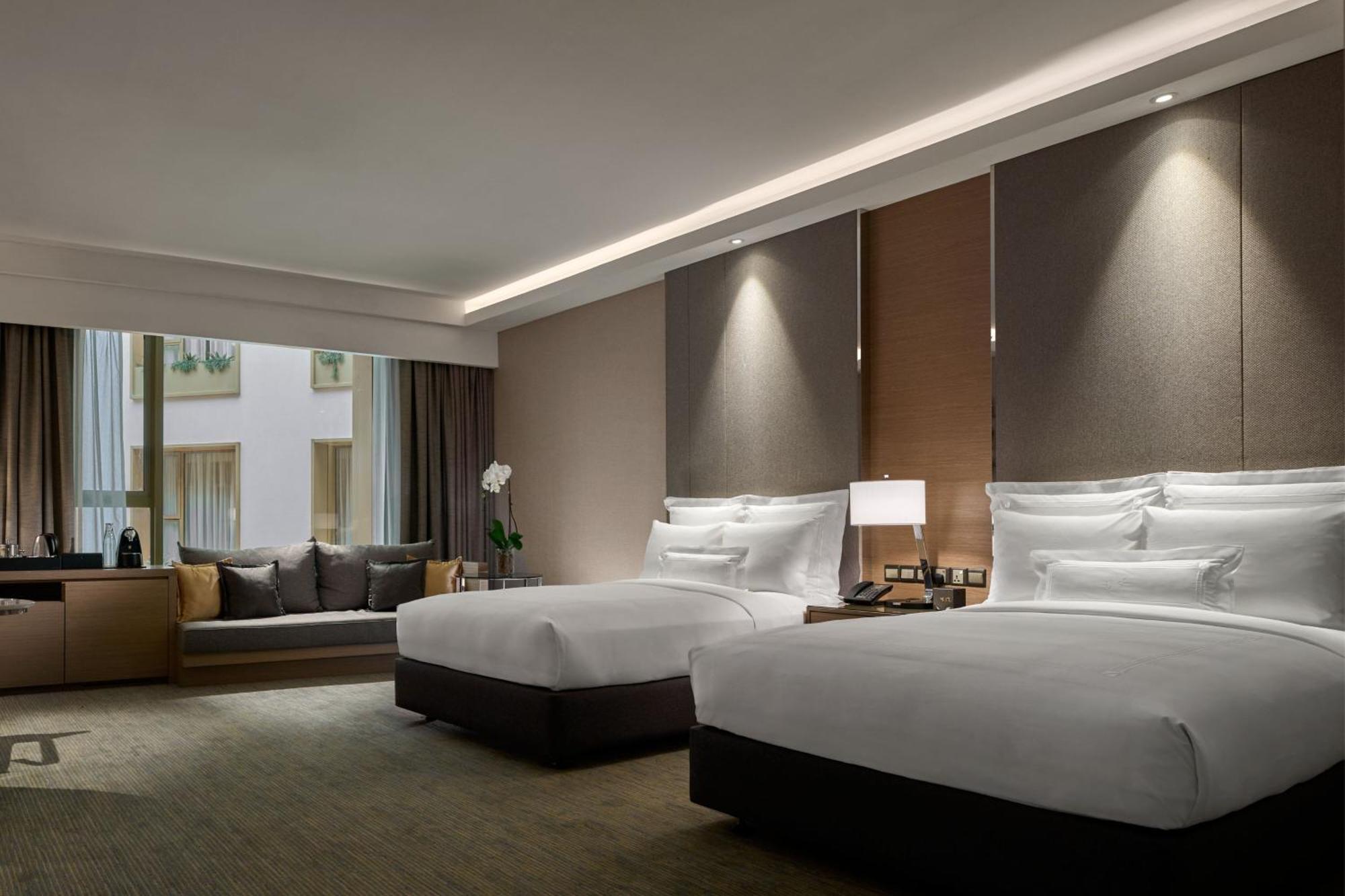 فندق جيه.دابليو ماريوت، كوالالمبور المظهر الخارجي الصورة The photo shows a modern hotel room featuring two beds with white linens. The walls are adorned with soft, muted colors and elegant lighting fixtures. There is a large window that allows natural light to enter, with a comfortable seating area beside 