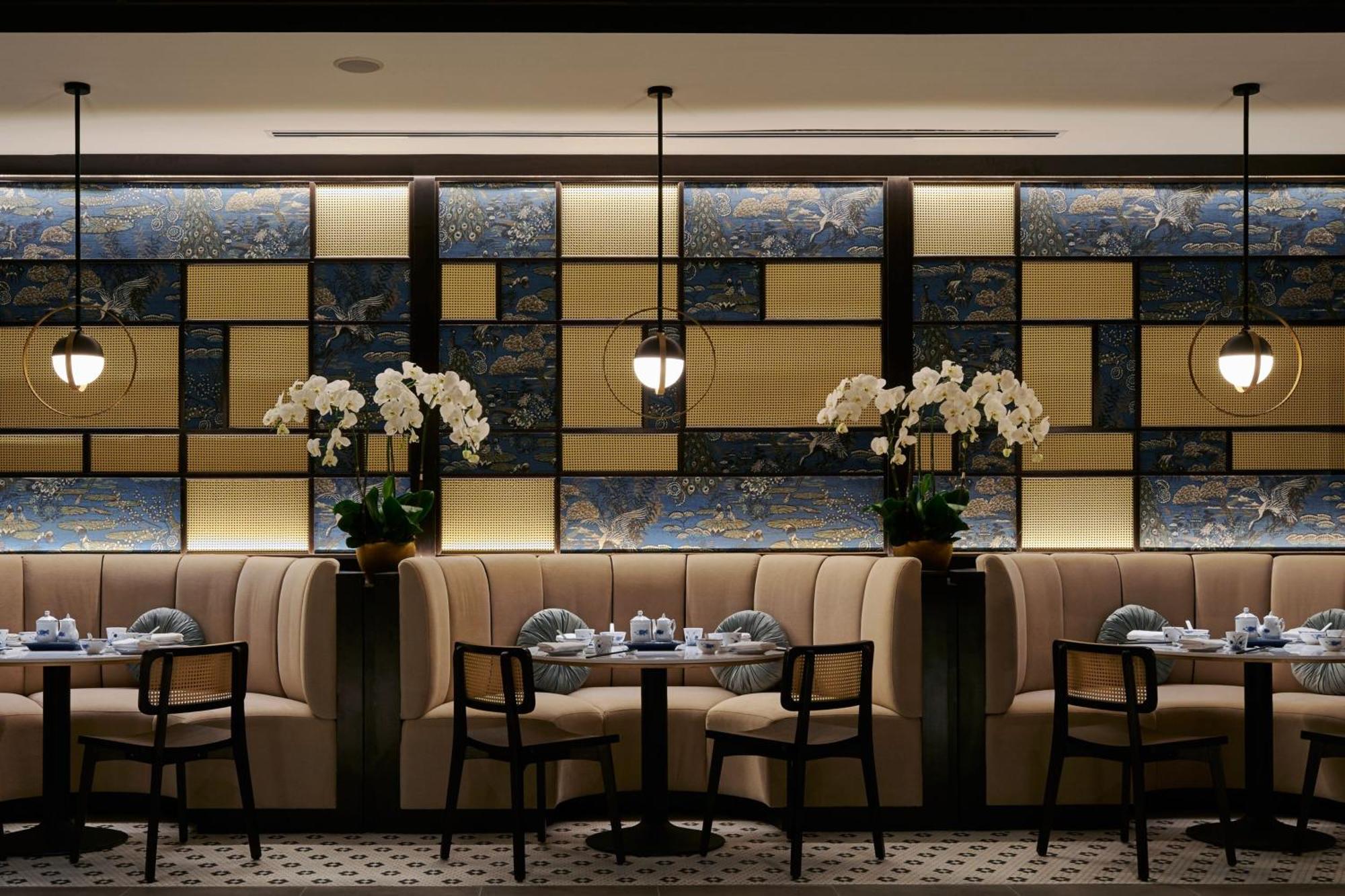 فندق جيه.دابليو ماريوت، كوالالمبور المظهر الخارجي الصورة The photo shows an elegant restaurant interior. The design features a stylish, modern aesthetic with tufted beige banquettes along the walls and dark wooden chairs. There are small round tables set with dishes and blue-and-white tableware. The backdr